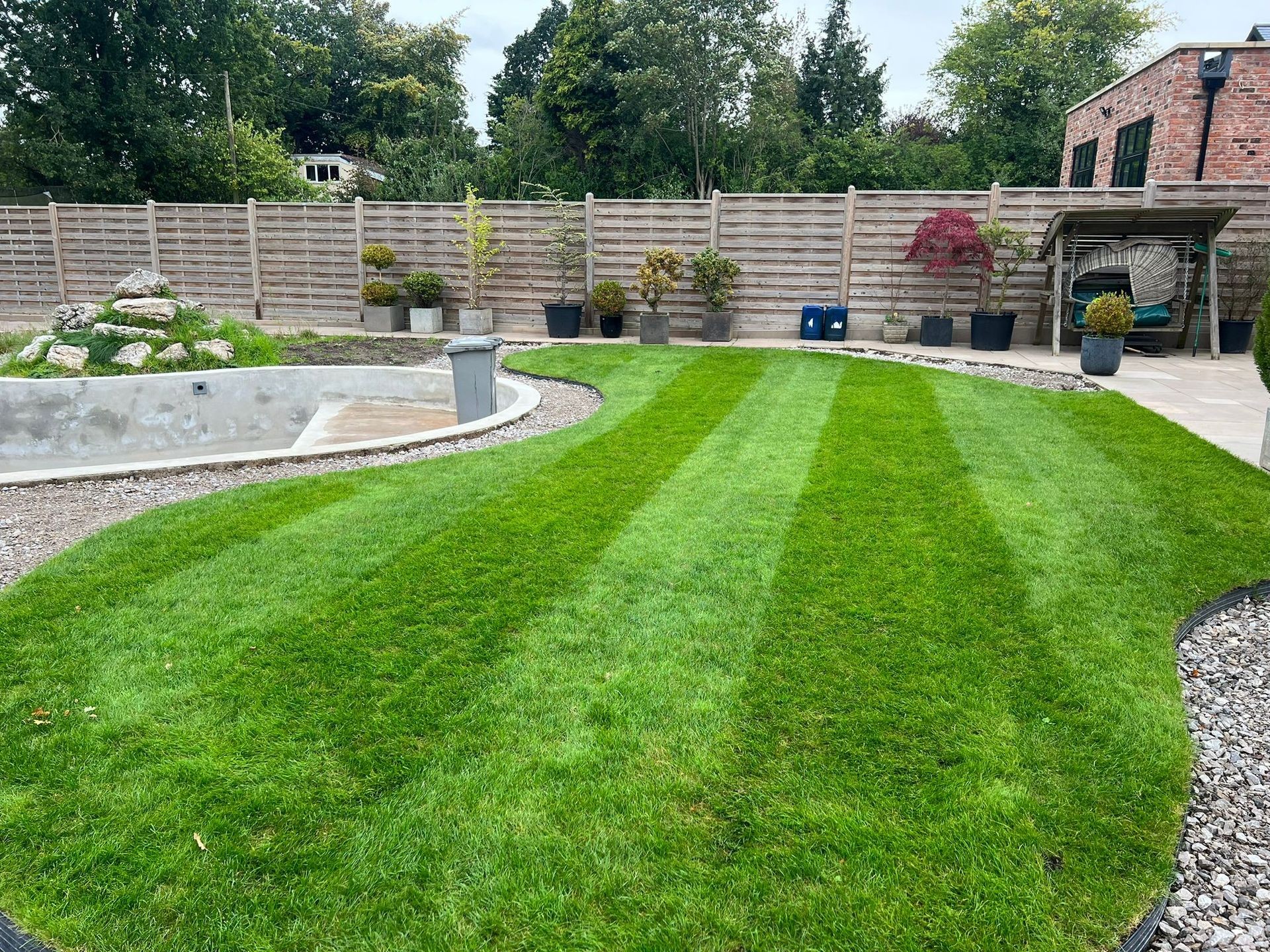 Well-manicured lawn with striped pattern, surrounded by potted plants and a wooden fence.